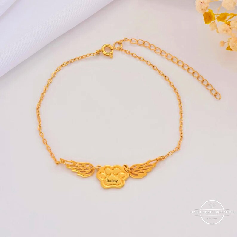 May include: Gold chain bracelet with a paw print charm with wings and the name "Bailey" engraved on it.
