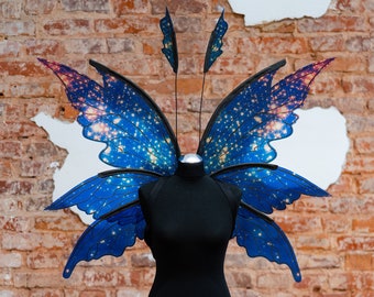 Könnte beinhalten: Eine schwarze Schaufensterpuppe mit einem Paar blauer und rosa Schmetterlingsflügel mit einem Galaxie-Druck. Die Flügel sind an den Schultern der Schaufensterpuppe befestigt.