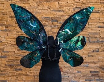 May include: A pair of large, green and black butterfly wings with gold accents, mounted on a black dress form.