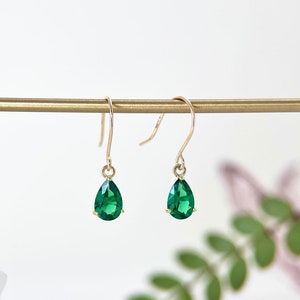 May include: A pair of gold teardrop earrings with green gemstone accents.