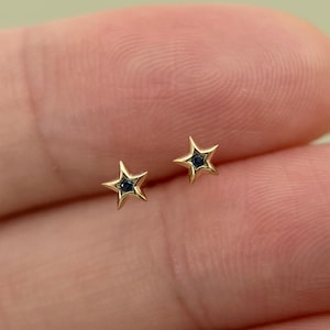 May include: A pair of gold star-shaped earrings with a small black gemstone in the centre of each star.