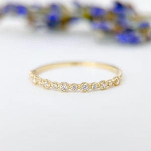Könnte beinhalten: Ein zarter Goldring mit einer Reihe kleiner, klarer Diamanten in einer Zargenfassung.