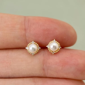 Op de afbeelding: Een paar gouden oorbellen met een parel en kleine diamanten in een vierkante zetting.