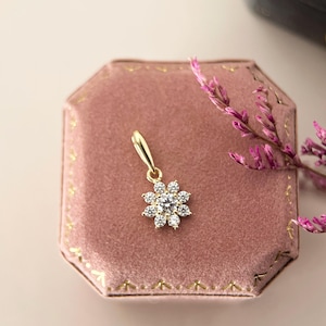 May include: A gold pendant featuring a central round clear stone surrounded by eight smaller round clear stones in a floral arrangement. The pendant has a polished gold bail at the top, designed to be attached to a chain for a necklace.