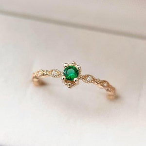 May include: A delicate gold ring with a small, round green gemstone surrounded by tiny diamonds. The ring has a delicate, ornate design.