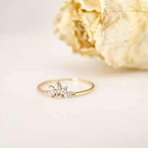 Puede incluir: Un delicado anillo de oro con cinco piedras preciosas claras de talla marquesa. El anillo tiene una banda delgada y pulida, y las piedras est&aacute;n dispuestas en un dise&ntilde;o floral o de corona. El anillo est&aacute; sobre un fondo suave y neutro.