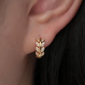 May include: Gold hoop earrings with a leaf design and clear cubic zirconia stones.
