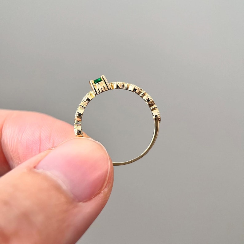 Puede incluir: Un anillo de oro con una peque&ntilde;a piedra preciosa verde engastada en la banda. El anillo tiene un dise&ntilde;o texturizado.