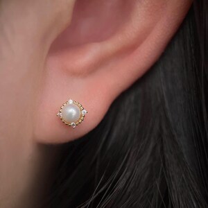 May include: A close-up of a pearl earring with a gold setting and small diamonds. The earring is worn in a person's ear.