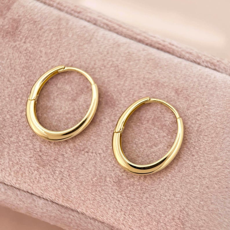 May include: A pair of gold oval hoop earrings. The earrings are smooth and have a polished finish.