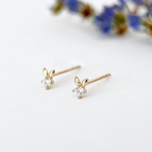 May include: A pair of gold earrings with a small clear stone and a leaf design.