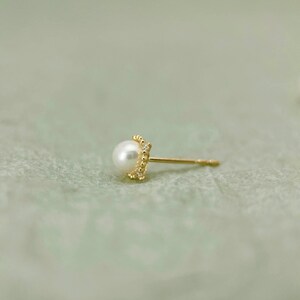May include: A single gold earring with a small pearl and a beaded border. The earring is on a white background.
