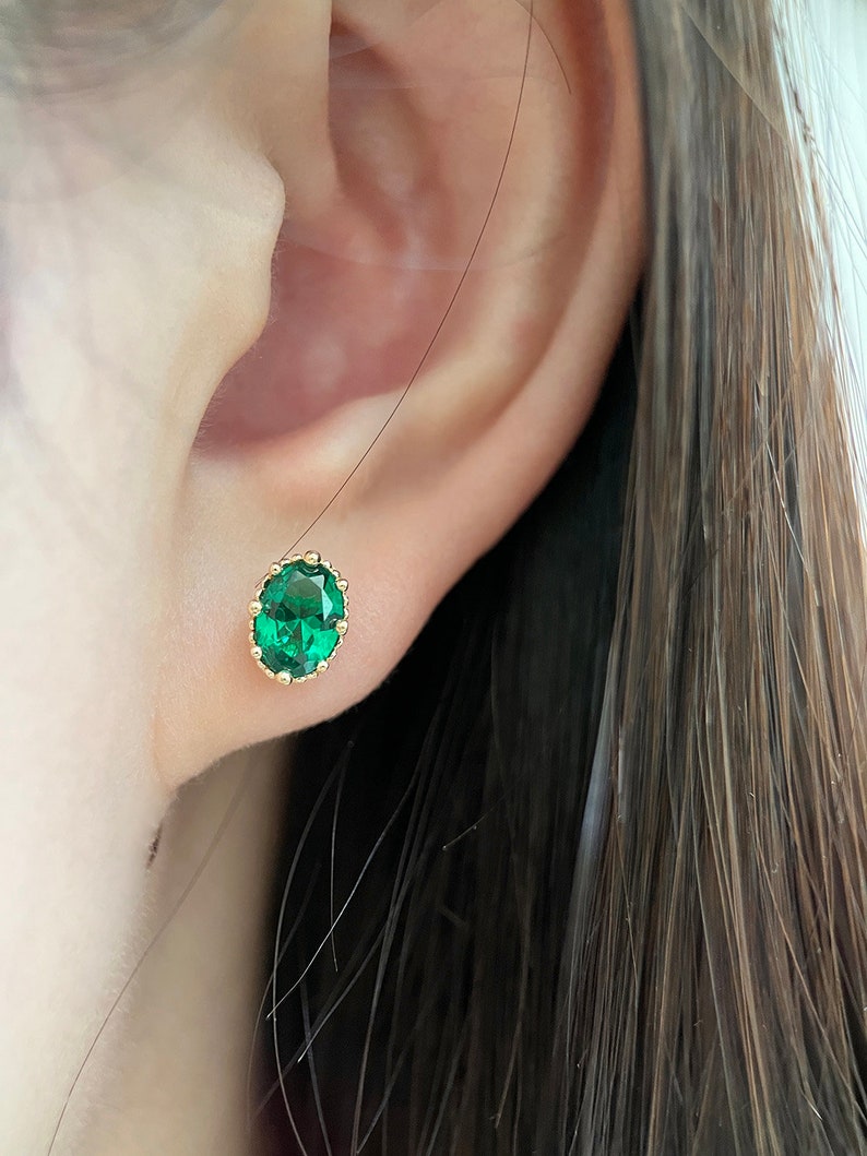Puede incluir: Un par de pendientes de oro con una piedra preciosa verde en un engaste de corona.