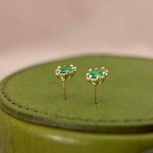 Puede incluir: Un par de pendientes de oro con piedras preciosas verdes engastadas en un dise&ntilde;o de corona.