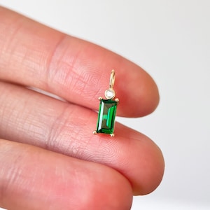 Puede incluir: Un dije de oro con una piedra preciosa verde en forma de esmeralda y un pequeño acento de diamante transparente.