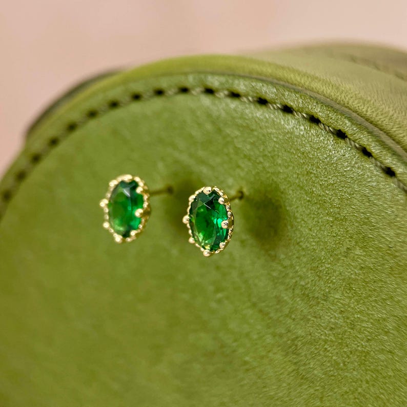 Puede incluir: Un par de pendientes de oro con piedras preciosas verdes ovaladas engastadas en un dise&ntilde;o de filigrana de oro.