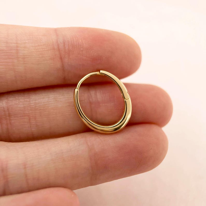 May include: A gold hoop earring with a smooth, polished finish. The hoop is oval shaped and has a seamless closure.