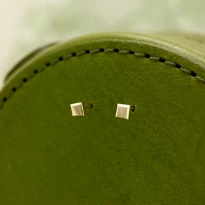 May include: A pair of small, square-shaped gold earrings on a green leather background.