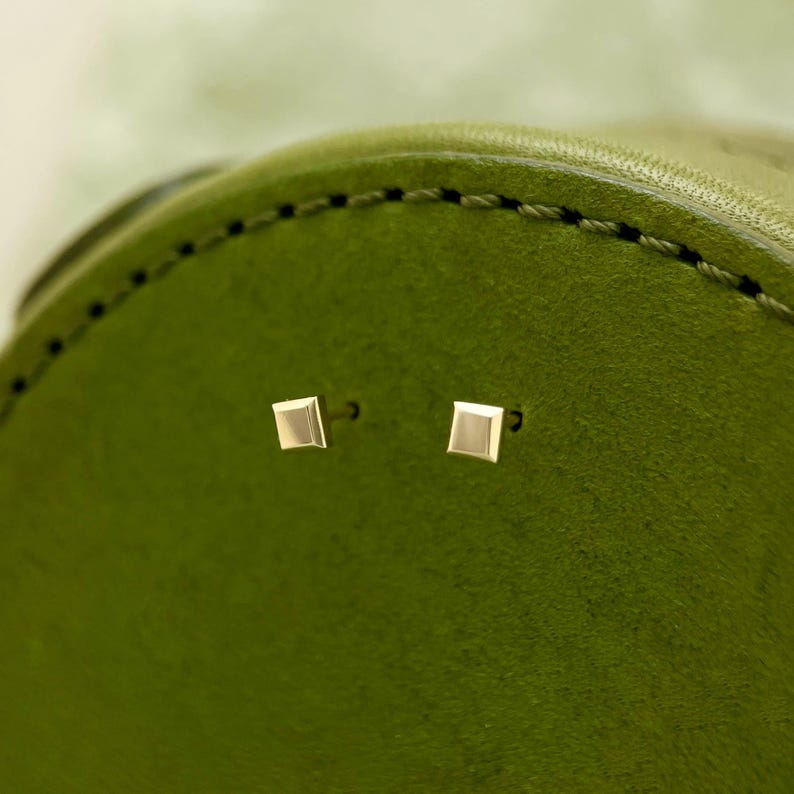 May include: A pair of small, square-shaped gold earrings on a green leather background.