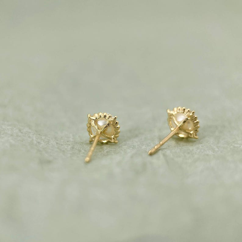 May include: A pair of gold earrings with a pearl center and a delicate, intricate design. The earrings are shown from the back, showcasing the post and butterfly clasp.