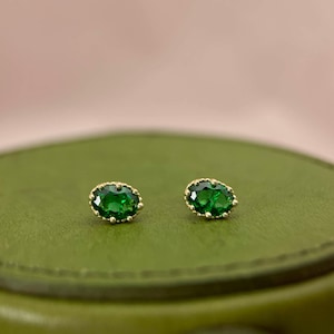 Puede incluir: Un par de pendientes de oro con piedras preciosas verdes de forma ovalada engastadas en un delicado marco de oro.