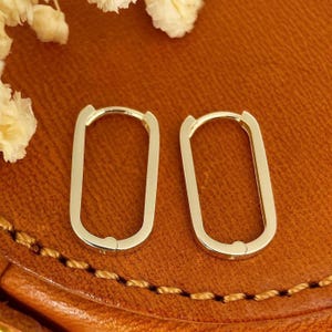 Könnte beinhalten: Ein Paar goldene ovale Creolen. Die Ohrringe sind schlicht und elegant und eignen sich hervorragend als Geschenk für jeden Anlass.