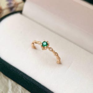 Puede incluir: Un delicado anillo de oro con una peque&ntilde;a piedra preciosa verde esmeralda rodeada de peque&ntilde;as piedras transparentes.