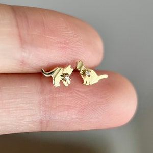 May include: A pair of gold cat stud earrings with a small diamond accent on each cat.