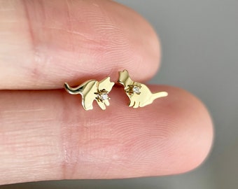 May include: A pair of gold cat stud earrings with a small diamond accent on each cat.