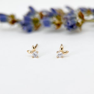 May include: A pair of gold earrings with a small, clear gemstone and a leaf design.