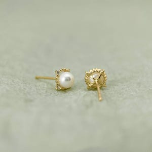 May include: A pair of gold earrings with a small pearl and a diamond accent. The earrings are shown from the side and the back.