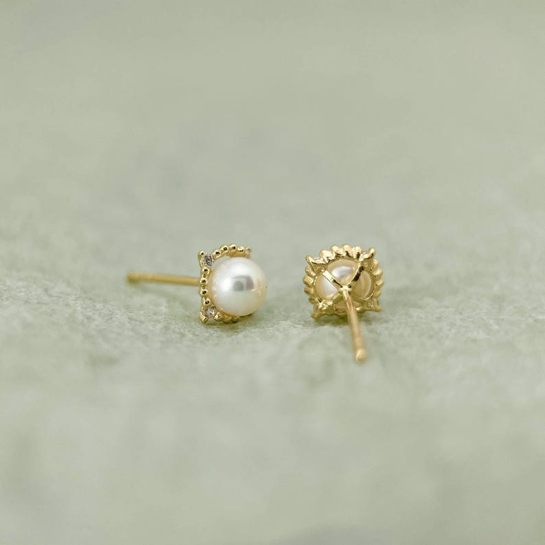 May include: A pair of gold earrings with a small pearl and a diamond accent. The earrings are shown from the side and the back.