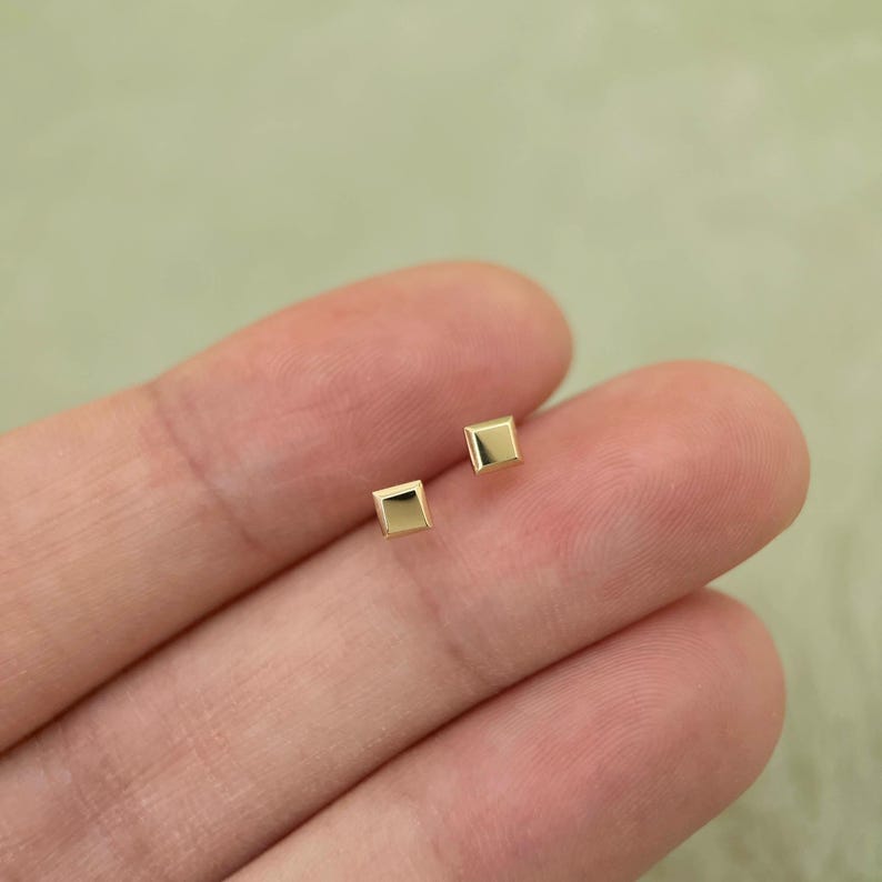 May include: A pair of small, square-shaped gold earrings.