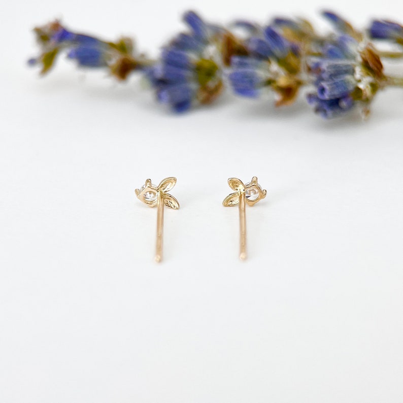 May include: A pair of gold stud earrings with a small clear stone in the centre of each earring. The earrings are shaped like a four-leaf clover.