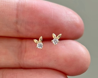 Puede incluir: Un par de pendientes de botón de conejo de oro con un pequeño strass transparente en el centro de cada conejo.