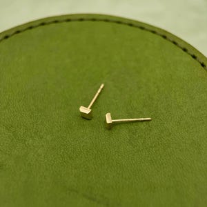 May include: A pair of gold square stud earrings on a green surface.