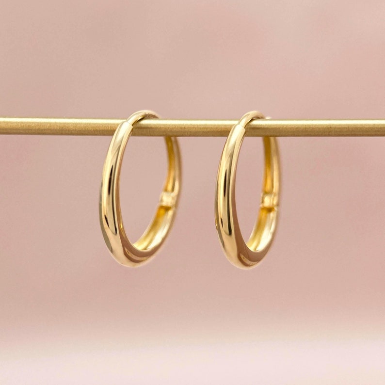 May include: A pair of gold hoop earrings hanging from a gold bar. The hoops are smooth and have a simple design.