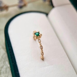Puede incluir: Un delicado anillo de oro con una peque&ntilde;a piedra preciosa verde y una banda de diminutos diamantes.