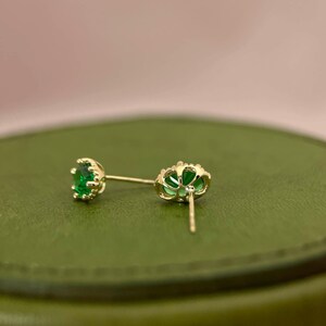 Puede incluir: Un par de pendientes de oro con piedras preciosas verdes. Los pendientes tienen un dise&ntilde;o delicado e intrincado.