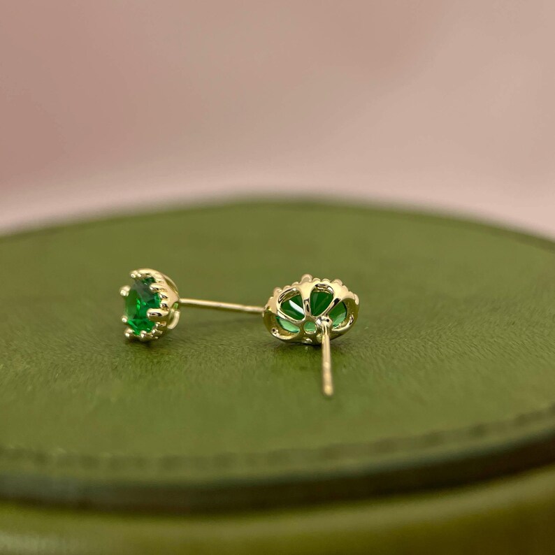Puede incluir: Un par de pendientes de oro con piedras preciosas verdes. Los pendientes tienen un dise&ntilde;o delicado e intrincado.