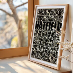 May include: A framed print with a black and white word cloud design featuring the word "Hatfield" in large letters. The word cloud includes various landmarks, businesses, and places of interest in Hatfield, England.