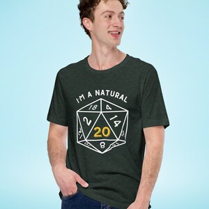 May include: A dark green t-shirt with a white graphic of a twenty-sided die with the number 20 highlighted in gold. The text "I'm a Natural" is printed above the die.