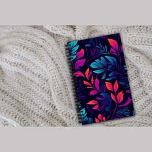 May include: A spiral bound notebook with a dark blue cover featuring a colourful floral pattern. The pattern includes pink, blue, and orange leaves.