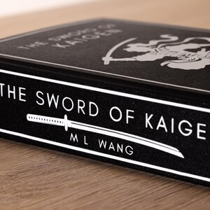 Puede incluir: Un libro negro titulado "The Sword of Kaigen" de M.L. Wang. El t&iacute;tulo y el nombre del autor est&aacute;n en blanco, junto con un gr&aacute;fico de espada estilizado. La portada del libro presenta una ilustraci&oacute;n blanca de una figura con una espada.