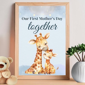 Könnte beinhalten: Ein gerahmter Druck mit einer Illustration von zwei Giraffen, einer erwachsenen und einer jungen, mit dem Text "Our First Mother's Day together" in Schreibschrift. Die Giraffen sind in Braun- und Beigetönen vor einem hellblauen Hintergrund.