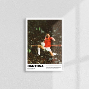 May include: A framed poster showing a soccer player in action, kicking a ball mid-air. The player is in a red jersey and white shorts. The poster includes the name "CANTONA" at the bottom, along with additional text.