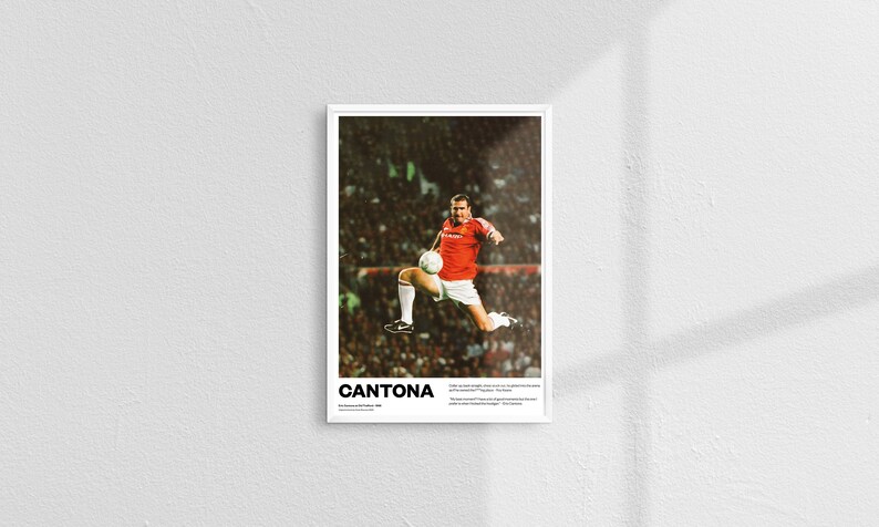 May include: A framed poster showing a soccer player in action, kicking a ball mid-air. The player is in a red jersey and white shorts. The poster includes the name "CANTONA" at the bottom, along with additional text.