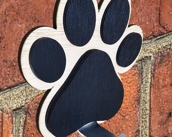 May include: Wooden paw print hook with a black painted finish and a metal hook. The hook is attached to a brick wall.