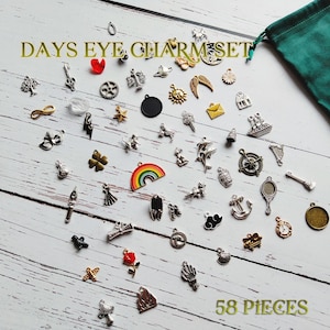 May include: A set of 58 silver and gold charm pendants, including a rainbow, a compass, a star, a heart, a key, a feather, a cloud, a mushroom, a flower, a dolphin, a crown, a bell, a sailboat, a castle, a bird, a butterfly, a sun, a crescent moon, a lightning bolt, a four-leaf clover, a scroll, a rose, a wand, a mirror, a seashell, a horseshoe, a tree, an infinity symbol, a gear, a  house, a  harp, an  anchor, a  clock, and a  fire. The charms are displayed on a white wooden surface with the text "DAYS EYE CHARM SET" and "58 PIECES" visible.