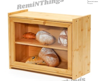 May include: A wooden bread box with a glass door and two shelves. The bread box is made of natural bamboo and has a light brown color. The bread box is filled with various loaves of bread.